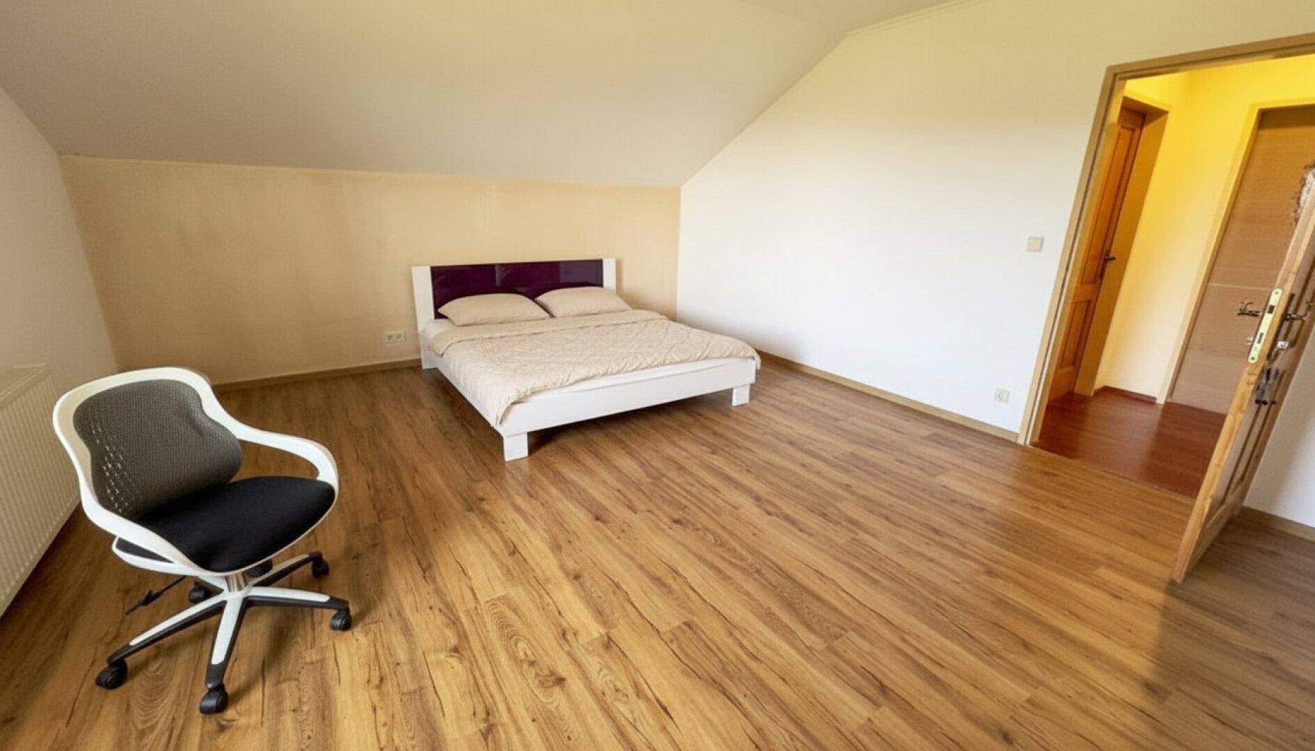 Schlafzimmer mit Laminatboden, Dachschräge und einem Bett mit lila Kopfteil.