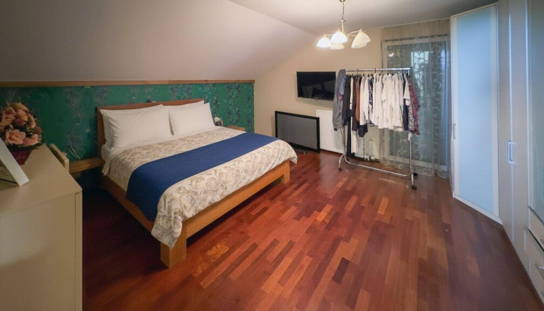 Schlafzimmer mit Holzboden, Dachschräge und einem Kleiderständer neben dem Bett.