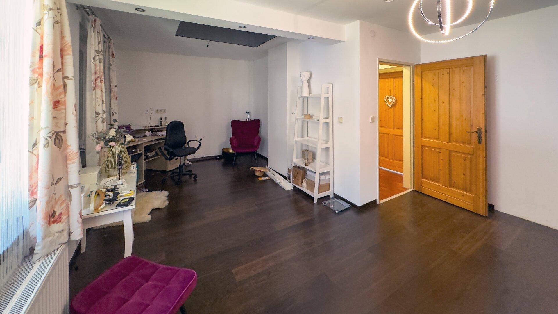 Geräumiges Arbeitszimmer mit dunklem Holzboden, floralen Vorhängen und viel Tageslicht.