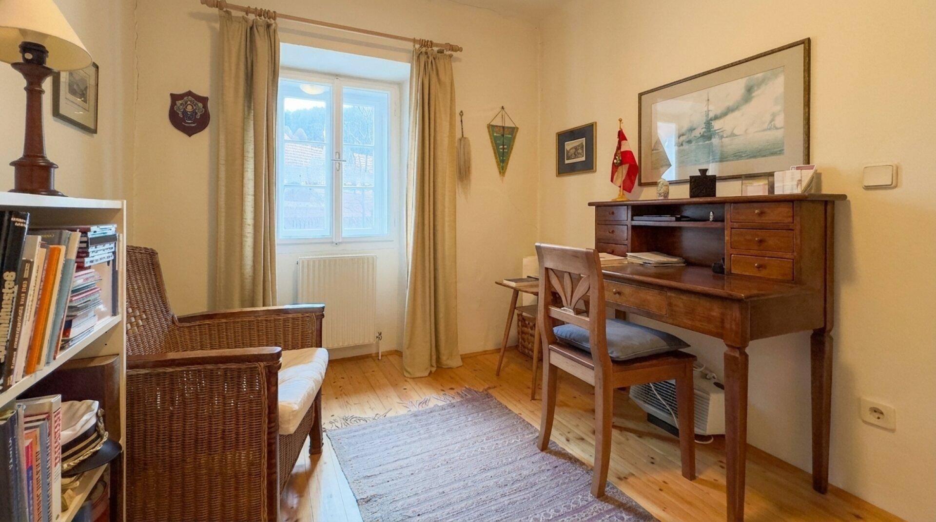 Kleines Arbeitszimmer mit Holzboden, Schreibtisch und Fenster mit Blick ins Grüne.