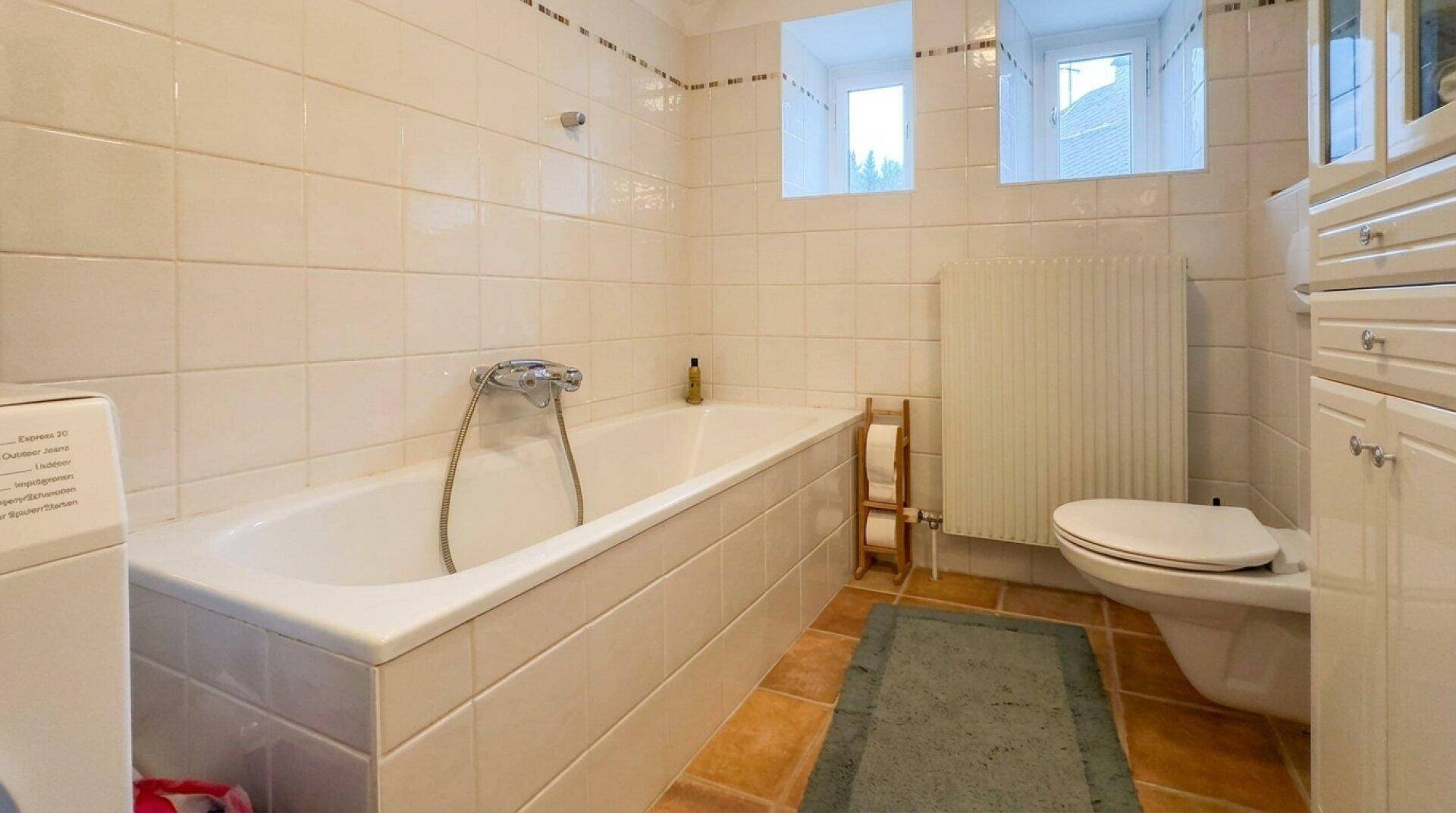 Badezimmer mit Badewanne, WC, Fliesen und Fenster für natürliche Belüftung.