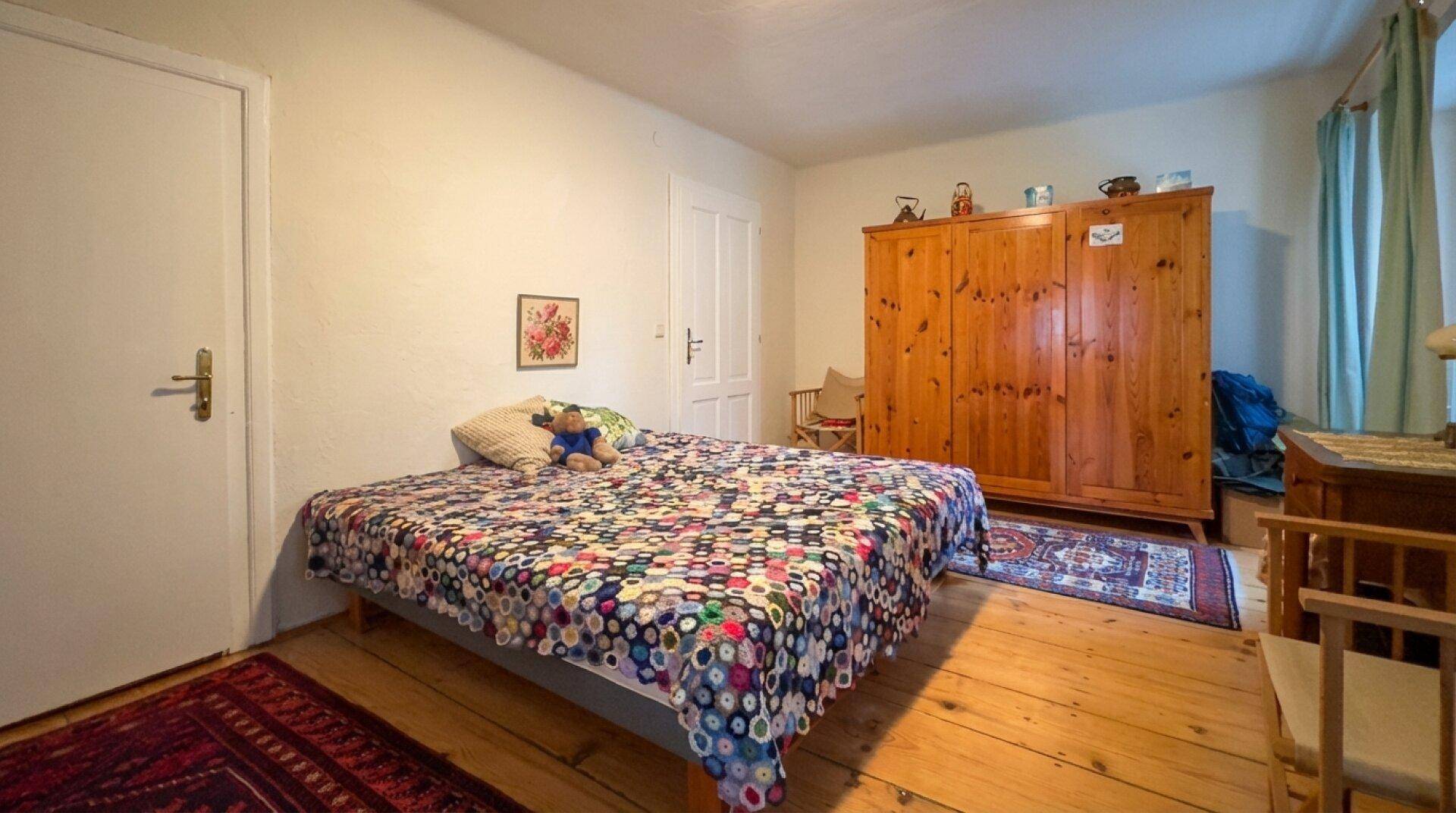 Helles Schlafzimmer mit Holzboden, großem Kleiderschrank und farbenfroher Bettdecke.