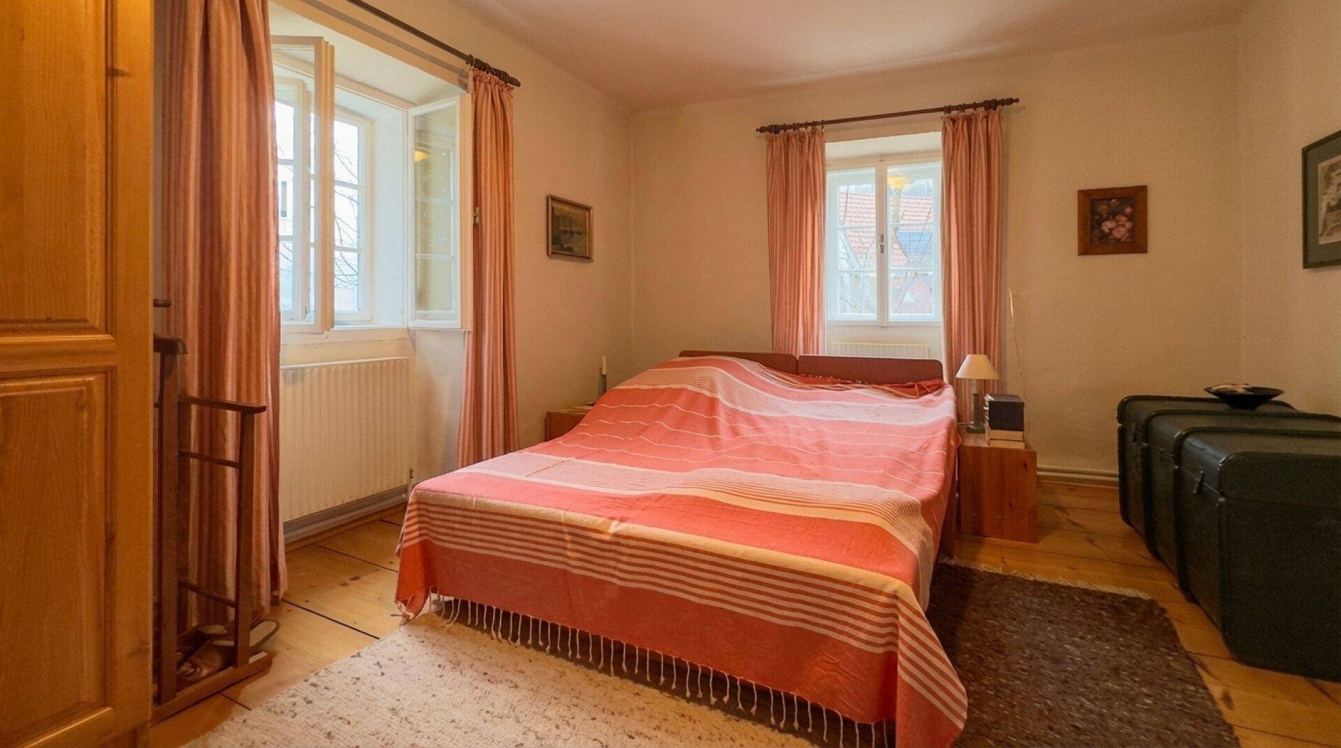 Schlafzimmer mit Holzboden, zwei Fenstern und traditioneller Einrichtung.