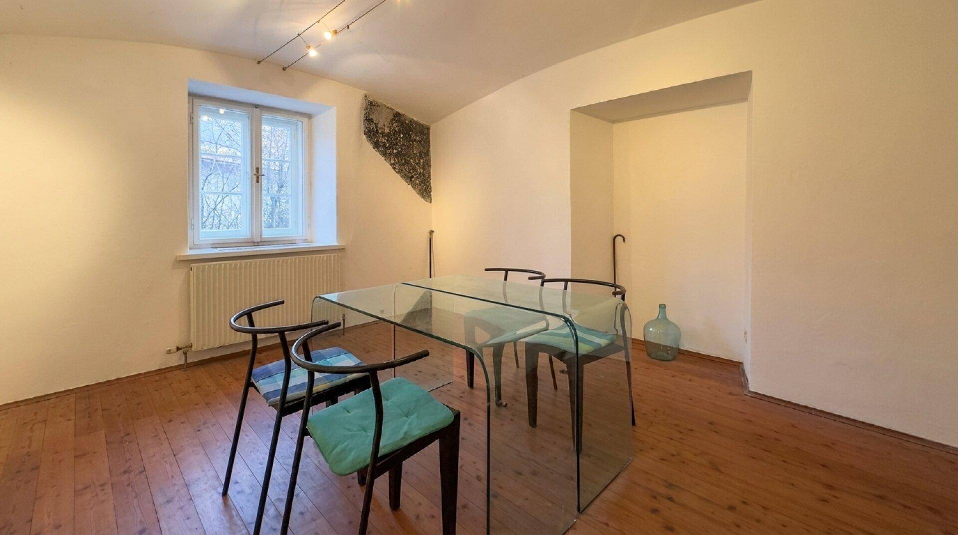 Heller Raum mit modernem Glastisch, Holzboden und einem Fenster.