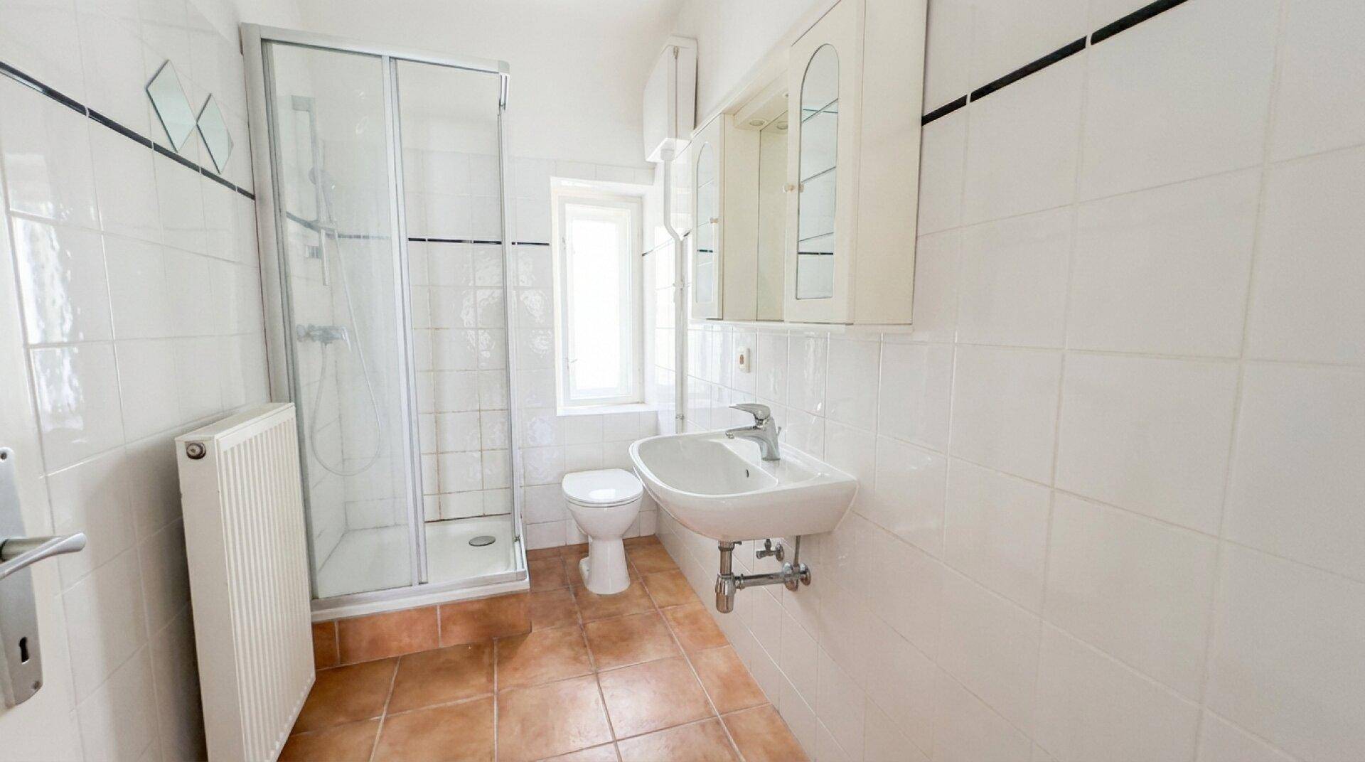 Kleines Badezimmer mit Duschkabine, WC, Waschbecken und Fenster.