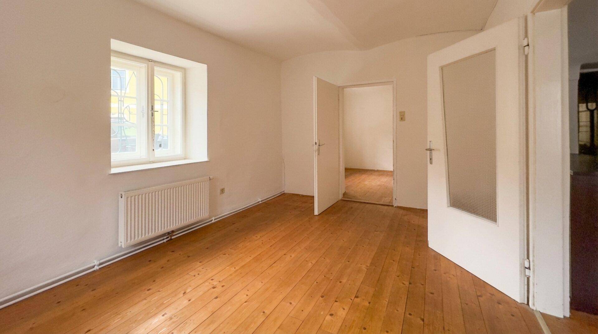 Leerer Raum mit Holzboden, weißen Wänden und zwei Türen.