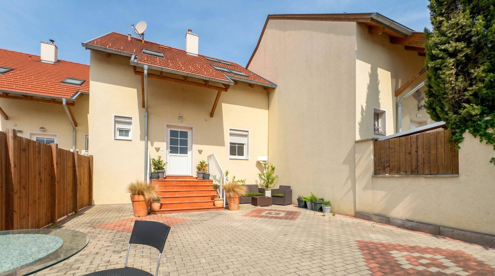 Gepflegter Hinterhof mit großer gepflasterter Fläche, Holzzaun und sonnigem Ambiente.