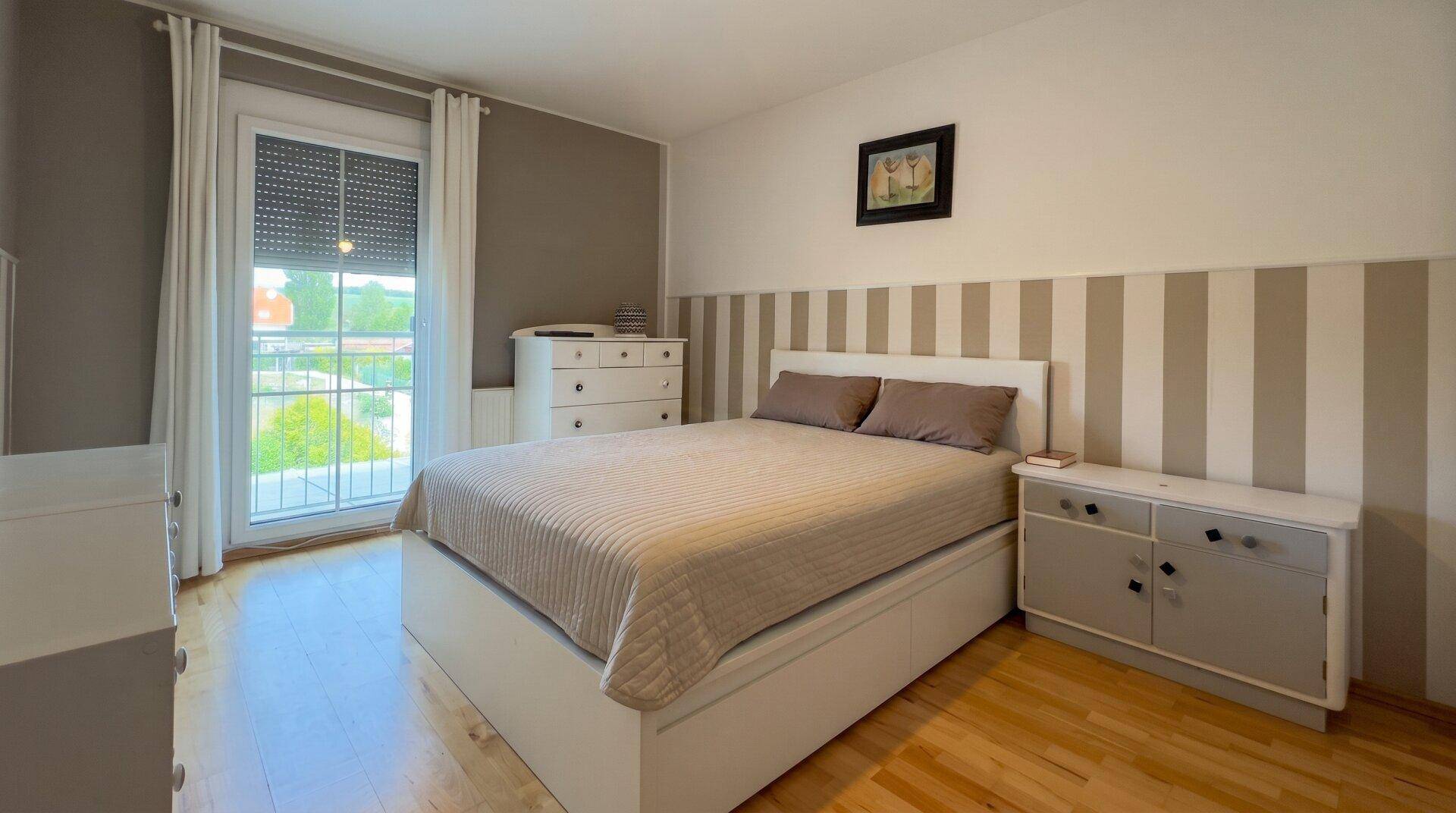 Helles Schlafzimmer mit Doppelbett, Holzfußboden und Zugang zu einem Balkon oder einer französischen Balkontür.
