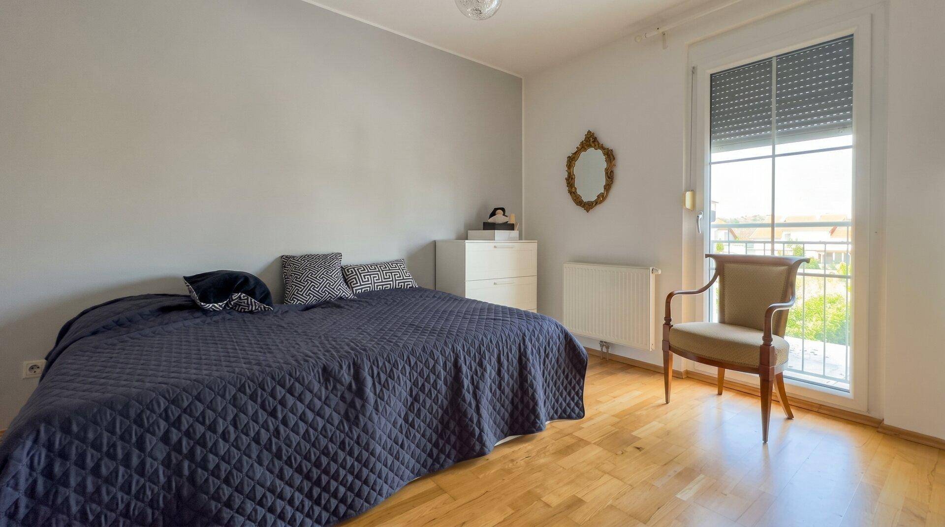Ruhiges Schlafzimmer mit Doppelbett, Holzparkett und großem Fenster für viel Tageslicht.