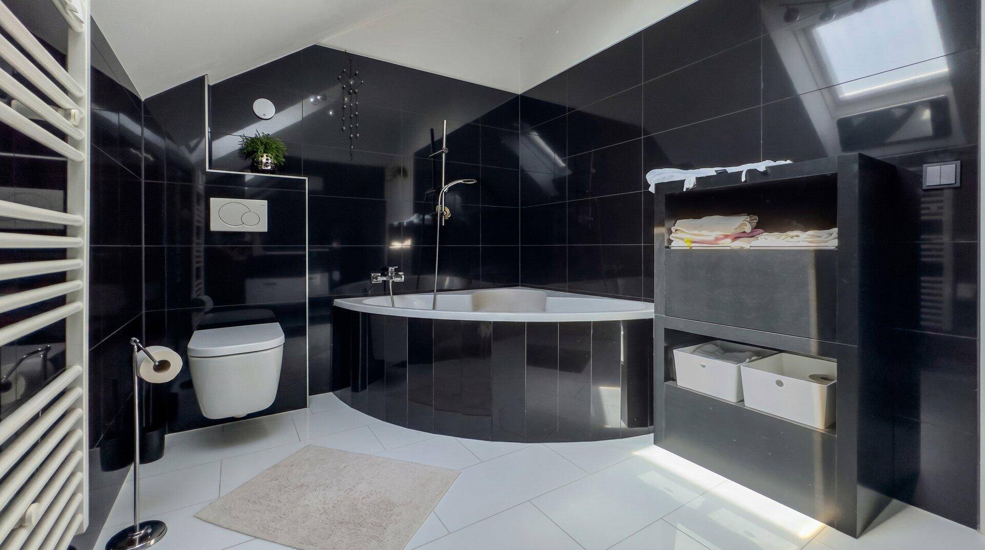 Modernes Badezimmer mit schwarzen Fliesen, runder Badewanne, wandhängendem WC und Dachfenster.
