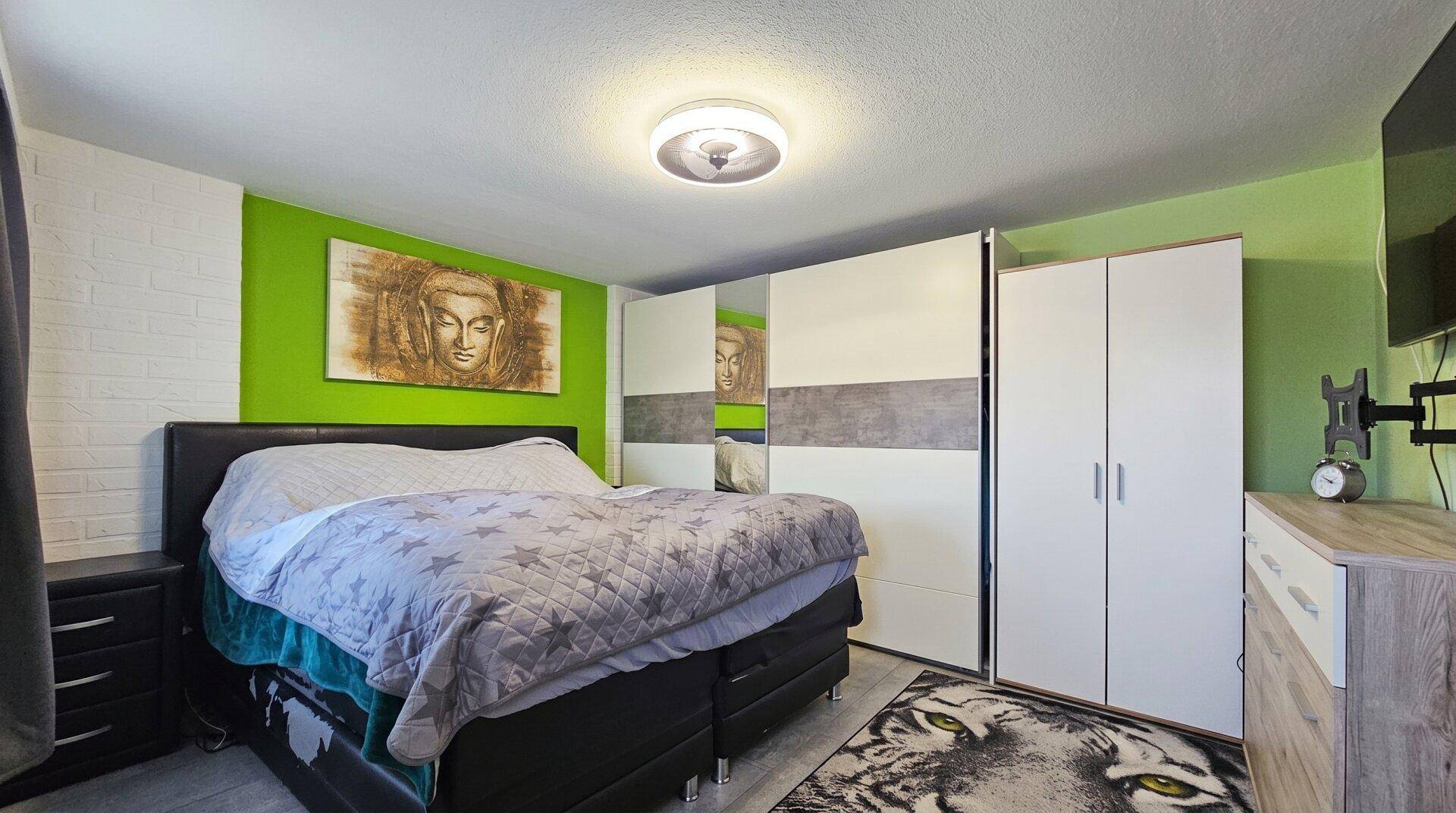 Schlafzimmer mit großem Bett, grüner Akzentwand und weißen Kleiderschränken.
