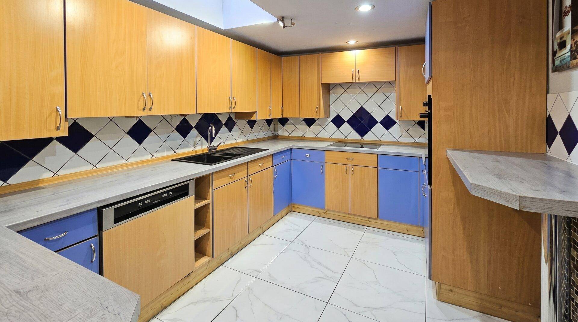 Küche mit Holzschränken, blauen Unterschränken und einem auffälligen Fliesenmuster an der Wand.