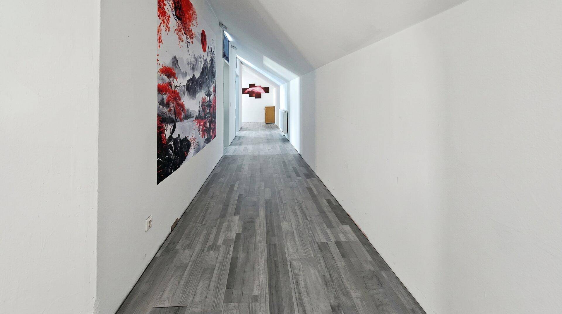 Langer Flur im Dachgeschoss mit schrägen Decken, Laminatboden und einem großen Wandbild.