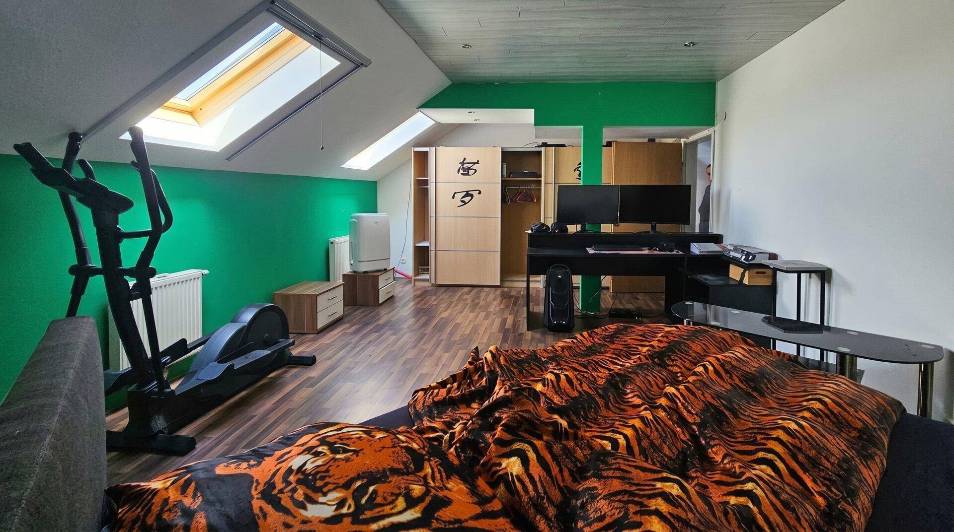 Vielseitiges Dachzimmer mit grünen Wänden, Bett, Schreibtisch und Fitnessgerät.
