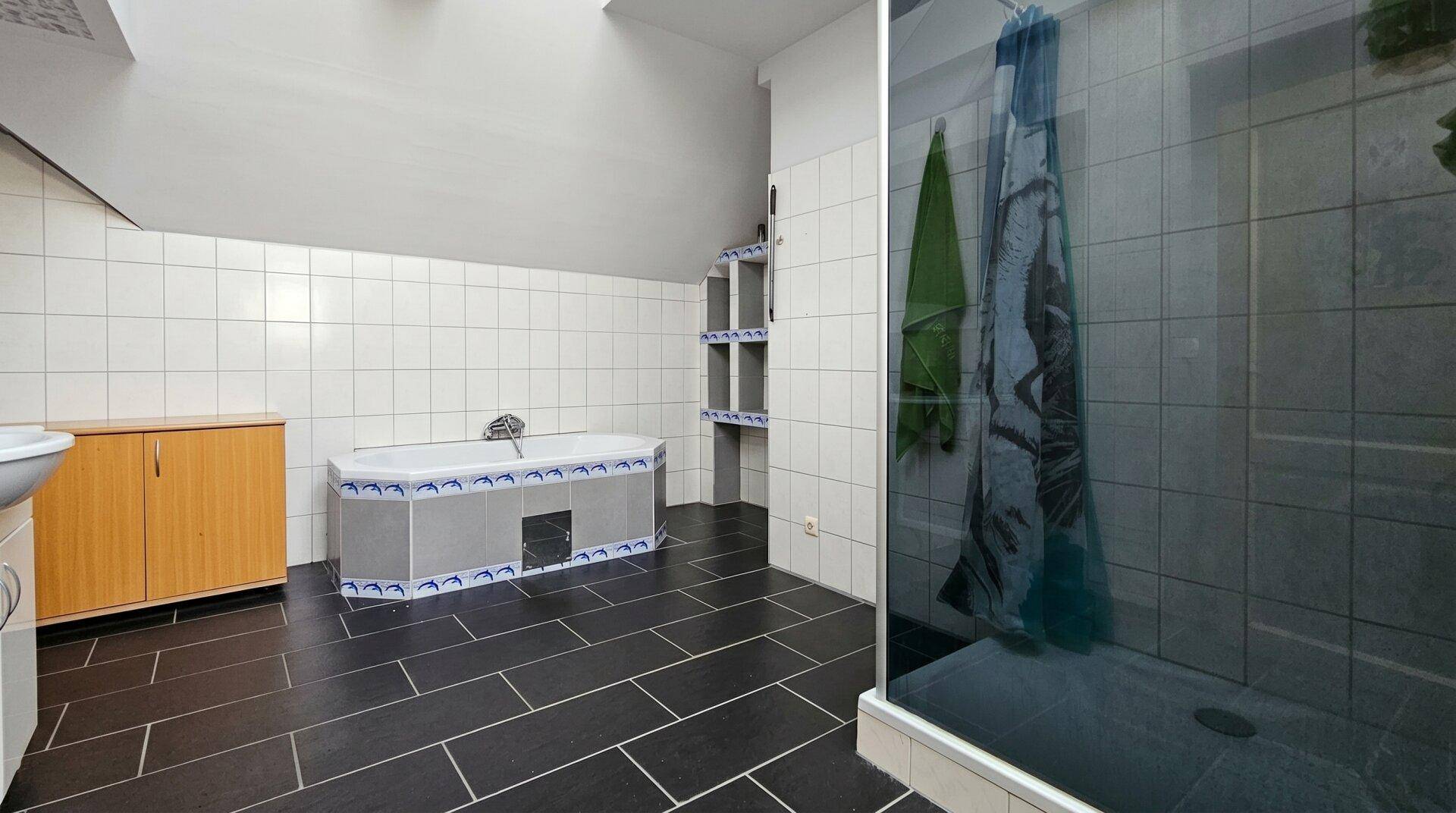 Badezimmer im Dachgeschoss mit weißen Wandfliesen, dunklen Bodenfliesen und Badewanne.