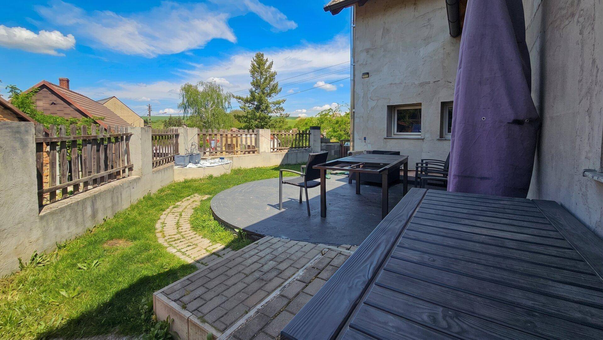 Sonniger Terrassenbereich mit Holztisch, Gartenmöbeln und Blick ins Grüne.