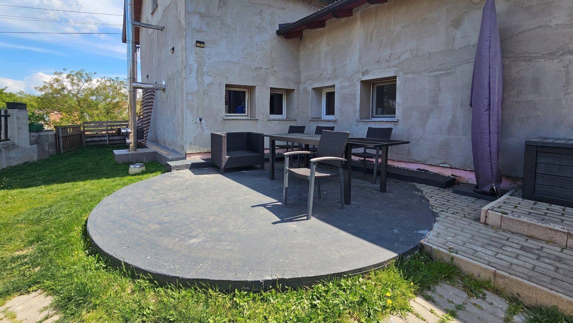 Runde Beton-Terrasse mit Esstisch und Stühlen im Freien, umgeben von Rasen.