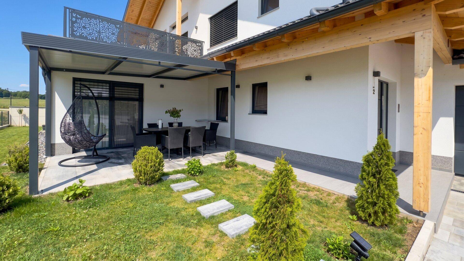Detailansicht der überdachten Terrasse mit Gartenmöbeln und einem Schaukelstuhl im gepflegten Garten.