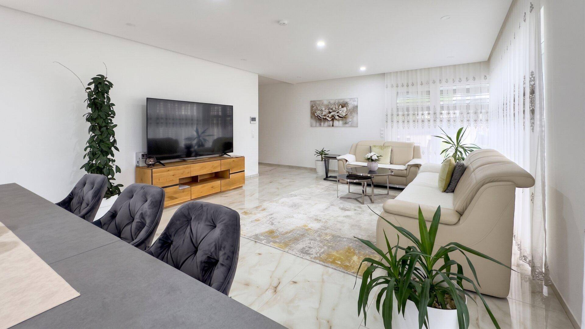 Geräumiges Wohnzimmer mit beigen Sofas, großem Fernseher und glänzendem Marmorboden.