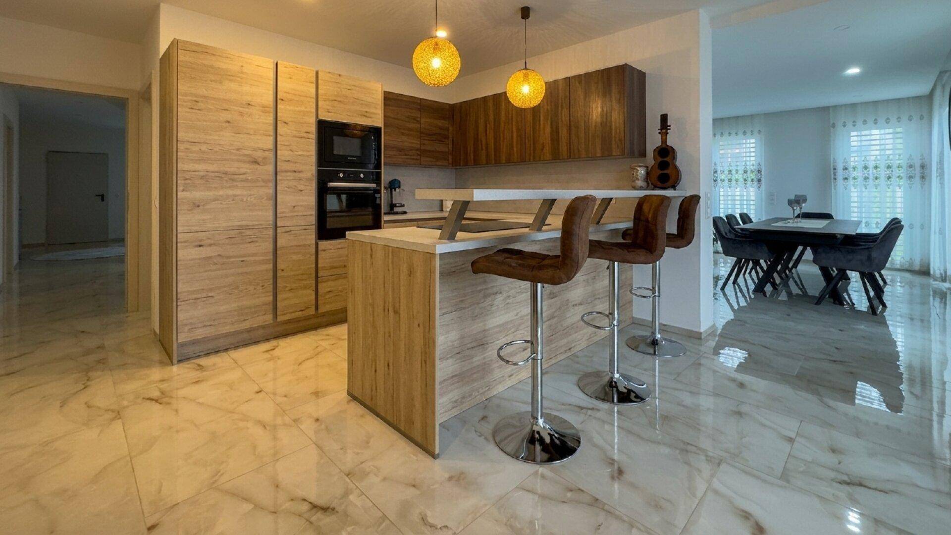 Moderne Küche mit Holzfronten, integrierten Geräten und einer Frühstücksbar mit Hockern.