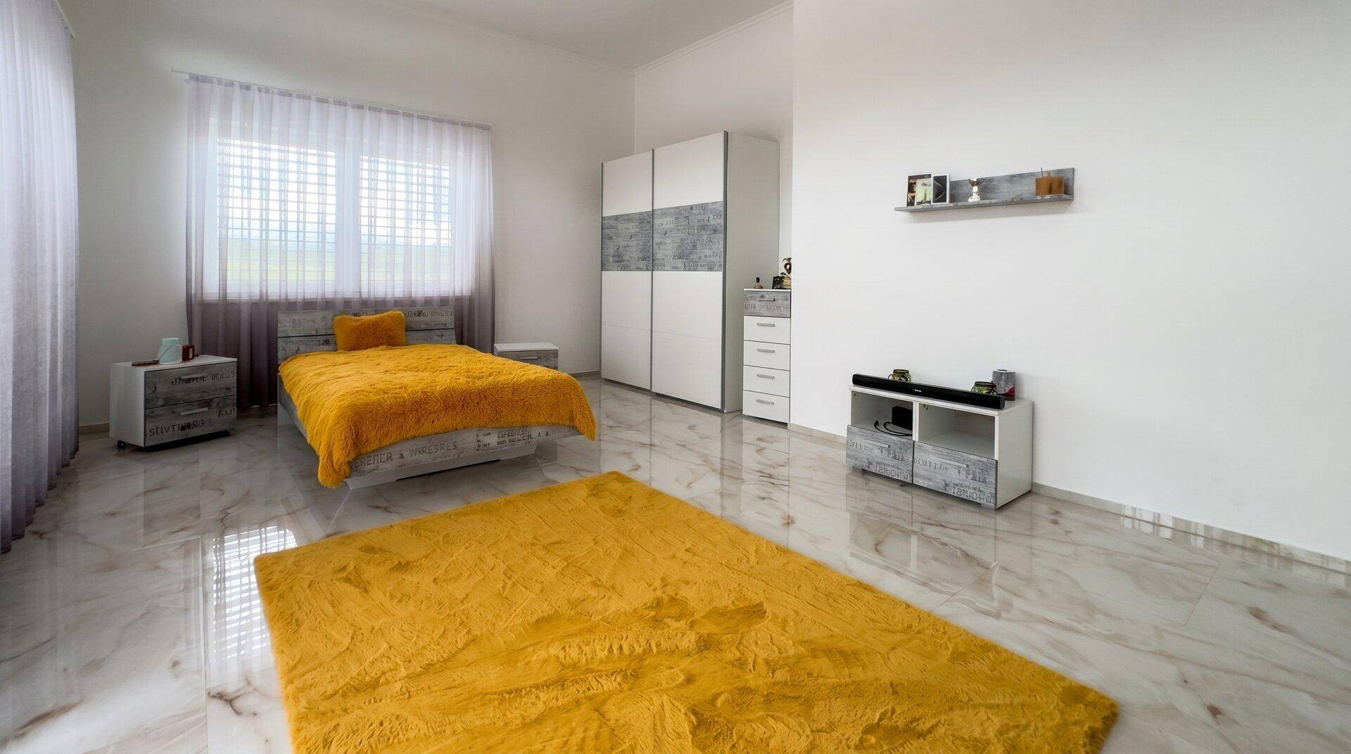 Geräumiges Schlafzimmer mit gelbem Teppich, weißem Kleiderschrank und Marmorboden.