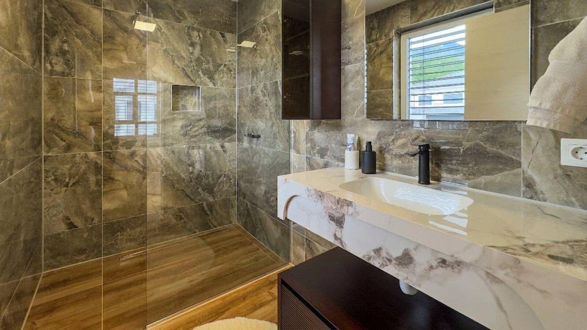 Elegantes Badezimmer mit dunklen Marmorfliesen, modernem Waschtisch und begehbarer Dusche.