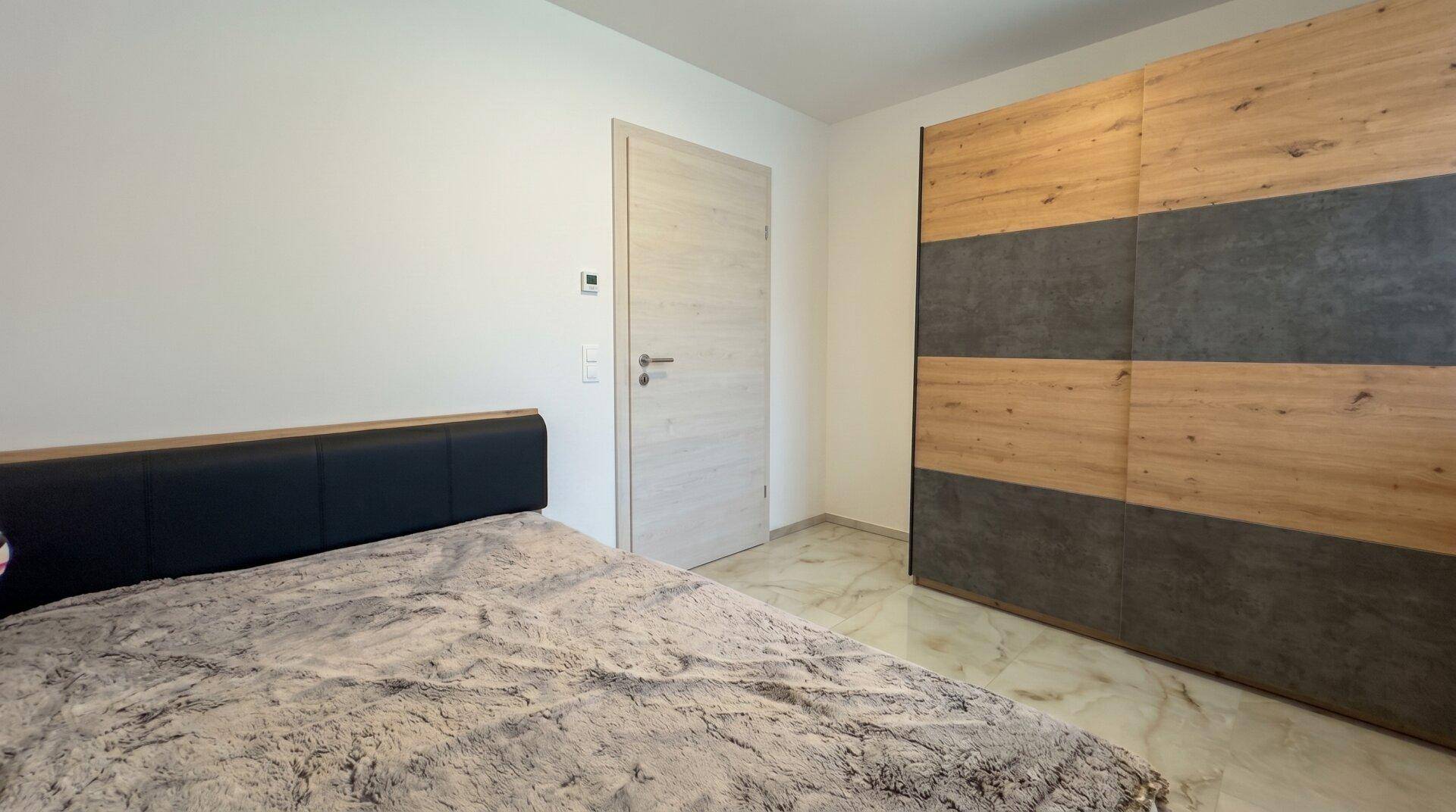 Schlafzimmer mit großem Bett und modernem Einbauschrank in Holz- und Betonoptik.