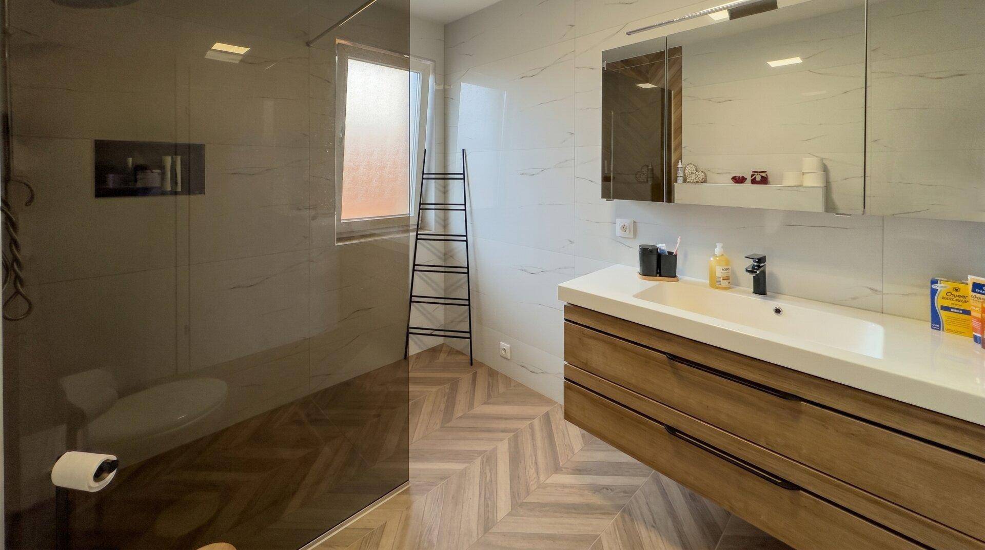 Helles Badezimmer mit Holzoptik-Fliesen, modernem Waschtisch und großer begehbarer Dusche.