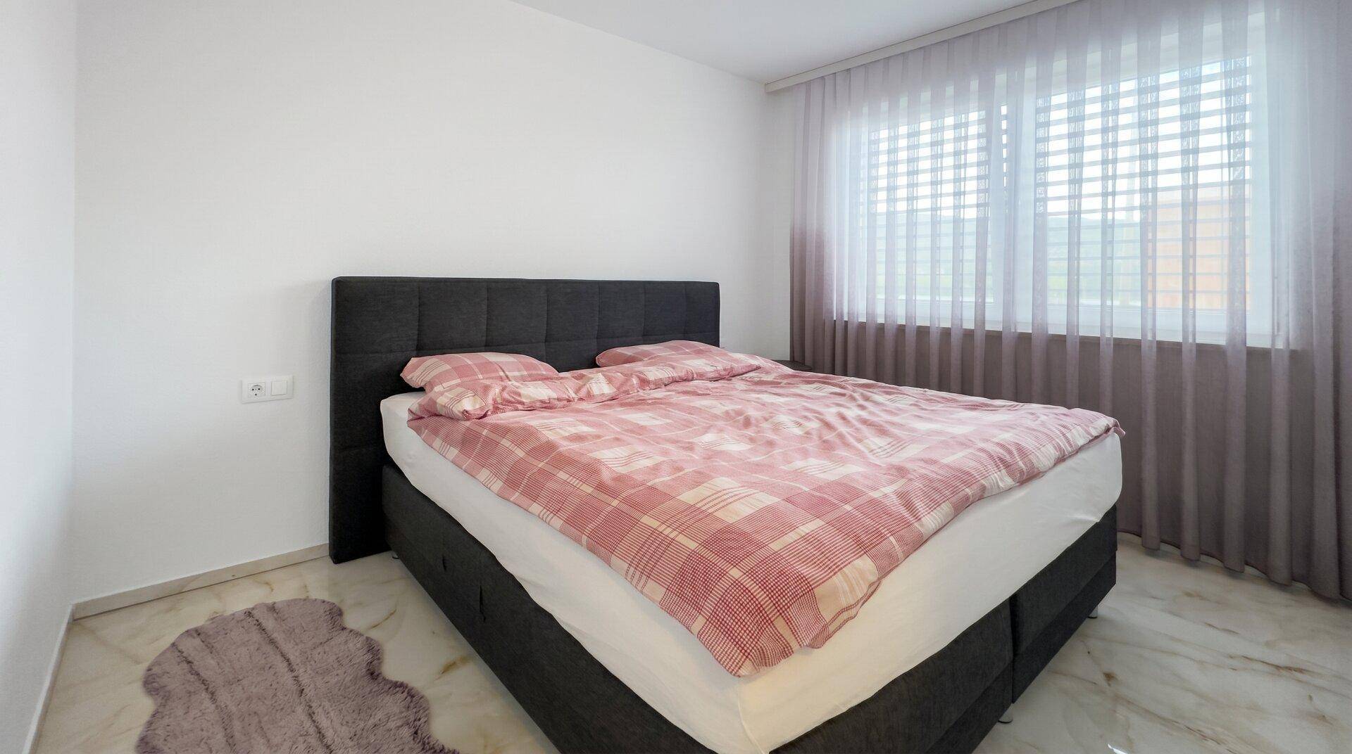 Gemütliches Schlafzimmer mit großem Bett, karierter Bettwäsche und Marmorboden.