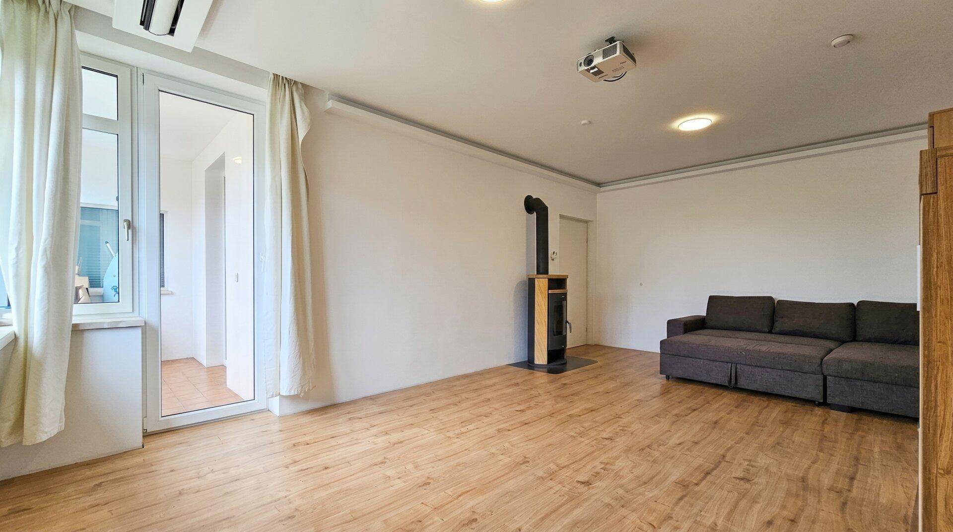 Gemütliches Wohnzimmer mit Kaminofen, Sofa und Zugang zu einem Balkon.