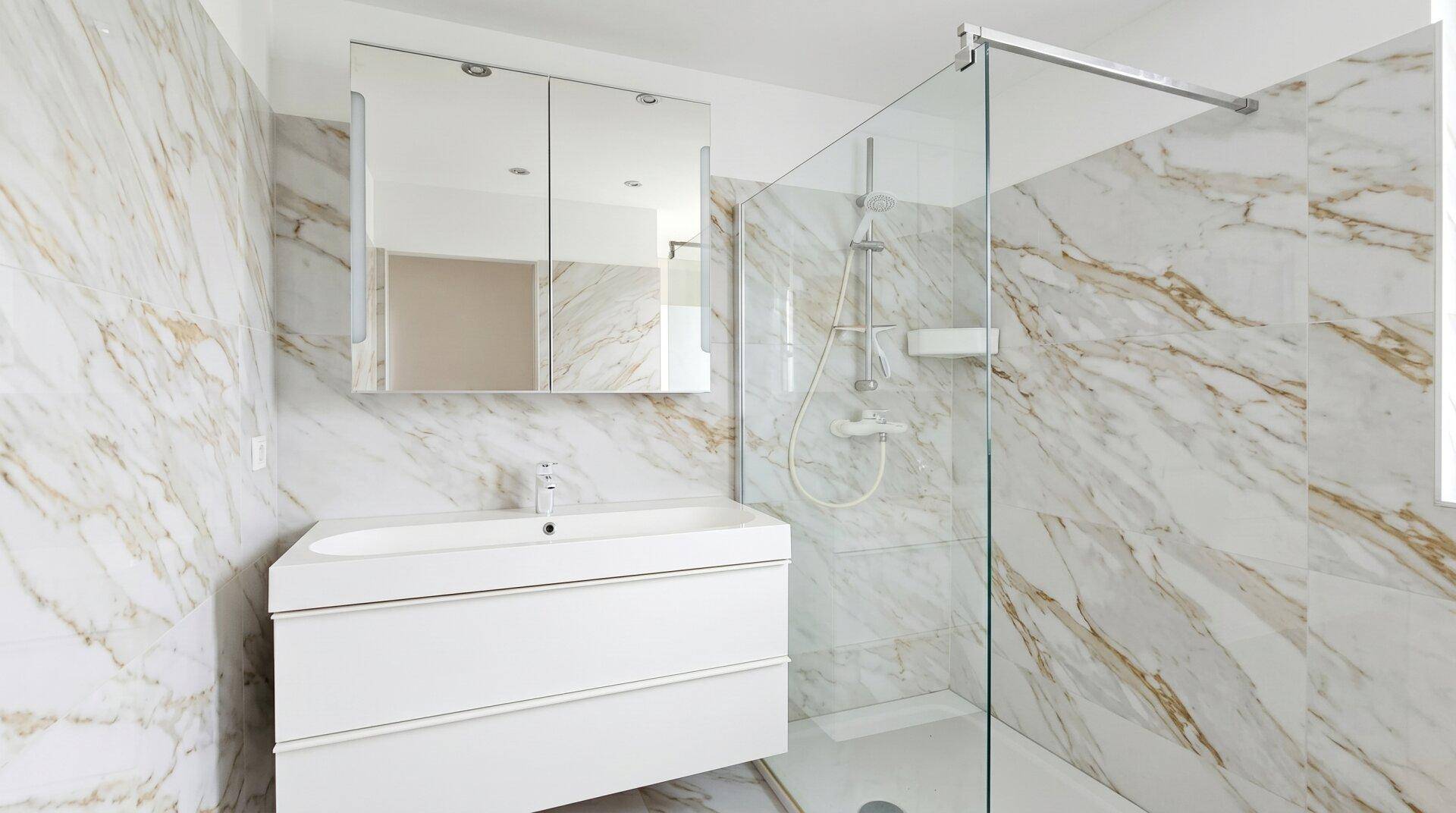Modernes Badezimmer mit Marmorfliesen, Duschkabine und Waschtisch mit Spiegelschrank.