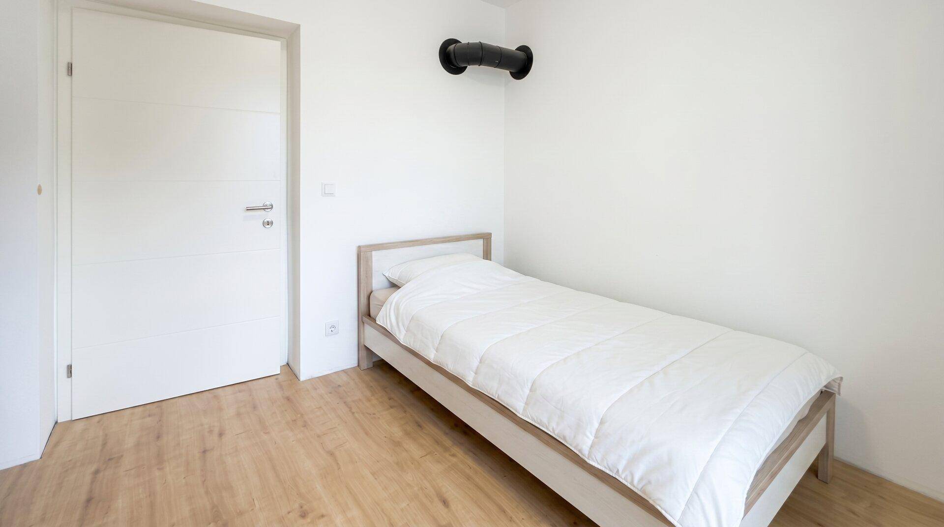 Helles Schlafzimmer mit Holzboden und Einzelbett, bietet eine einfache und saubere Einrichtung.