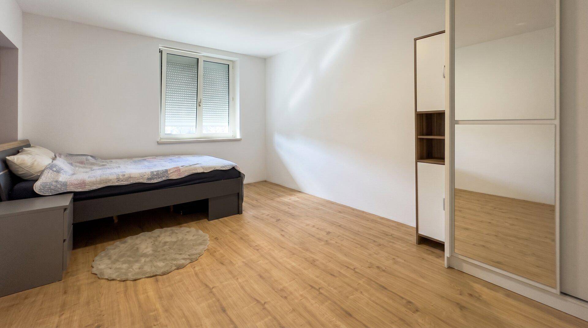 Schlafzimmer mit Holzboden, Einzelbett und Spiegelschrank, hell und funktional.