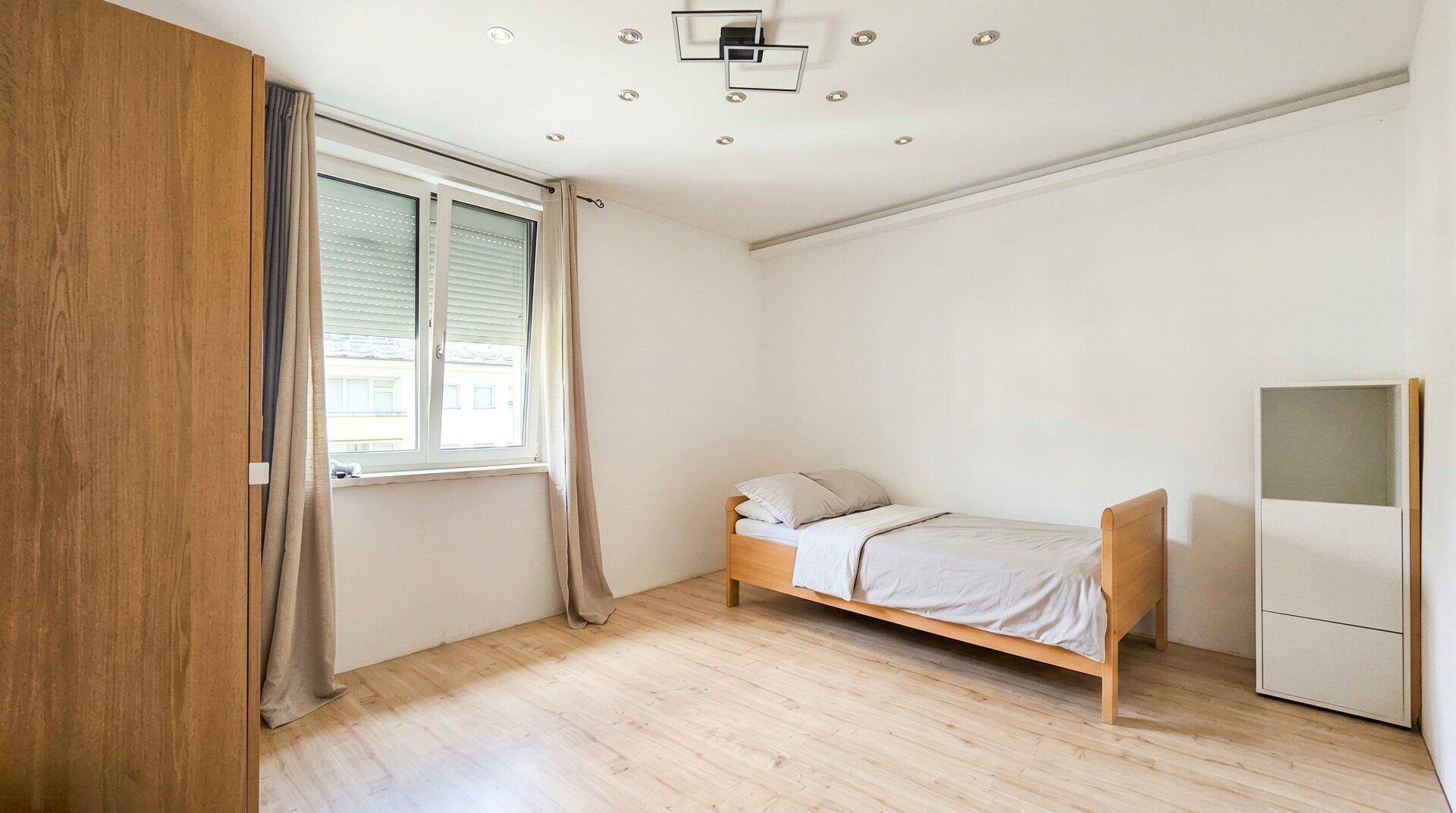 Schlafzimmer mit Holzboden, Einzelbett und Fenster mit Rollladen, hell und funktional.