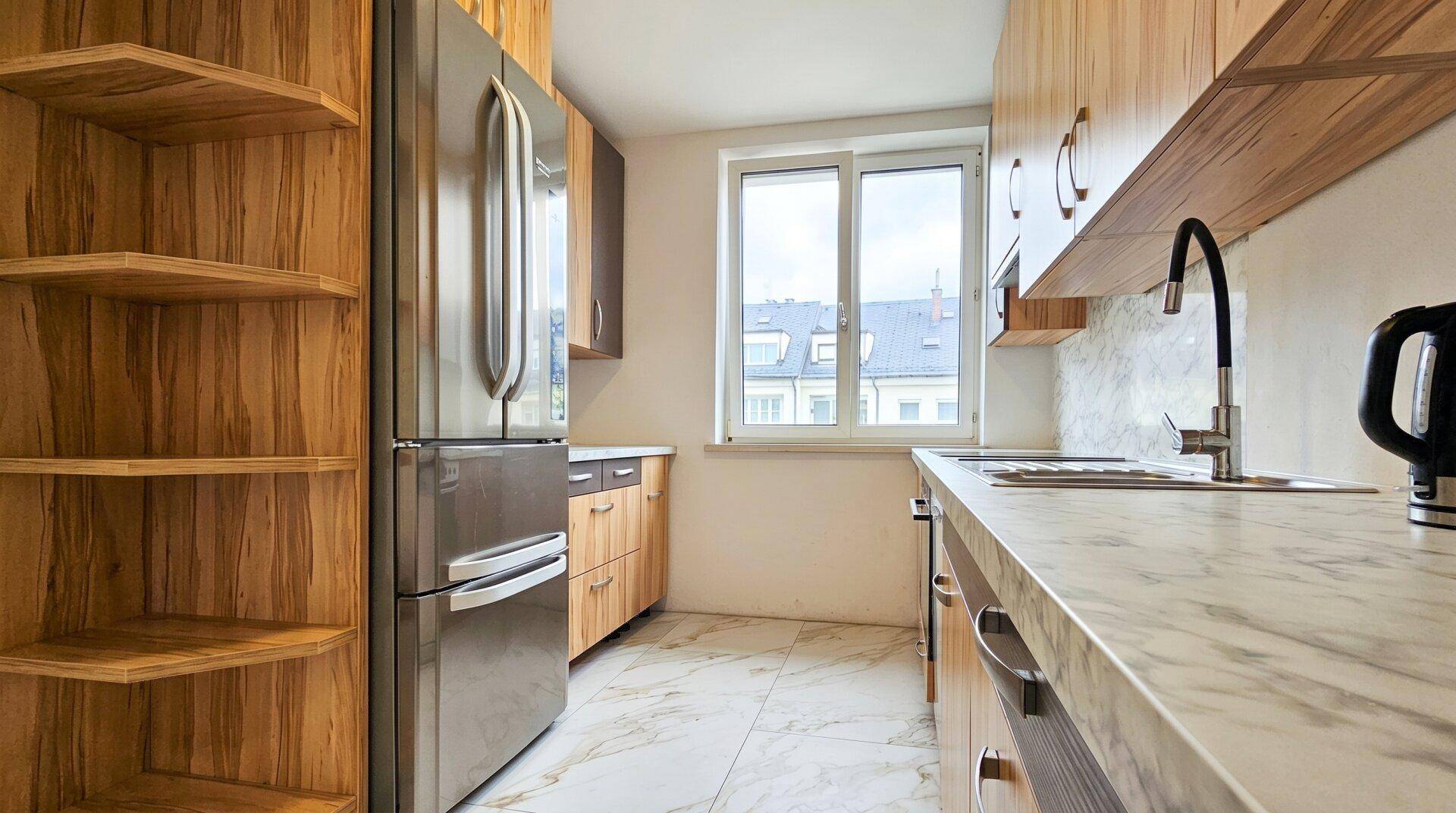 Helle Küche mit Holzregalen, Kühlschrank und Marmor-Arbeitsplatte, bietet viel Stauraum.