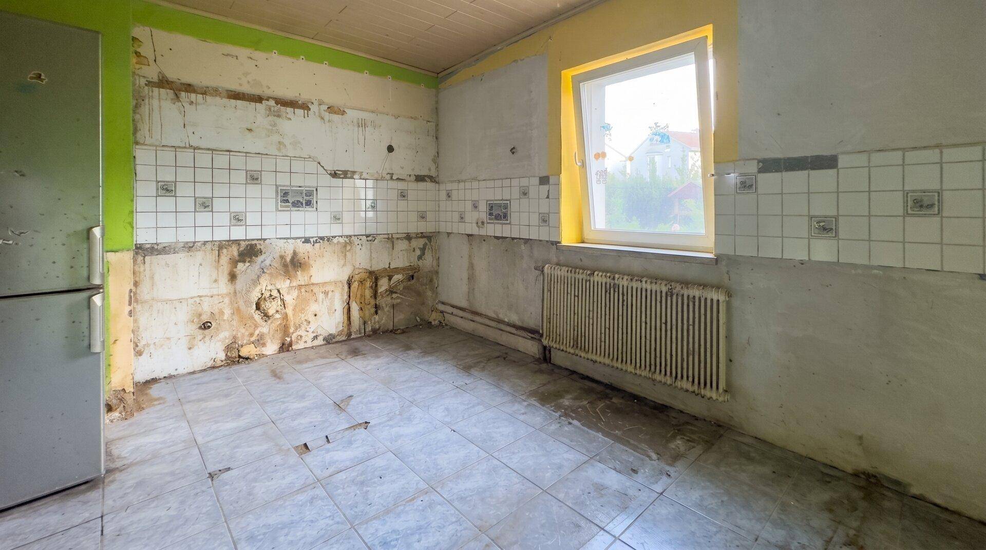 Renovierungsbedürftige Küche mit alten Fliesen, Fenster und leerem Raum für neue Einbauten.