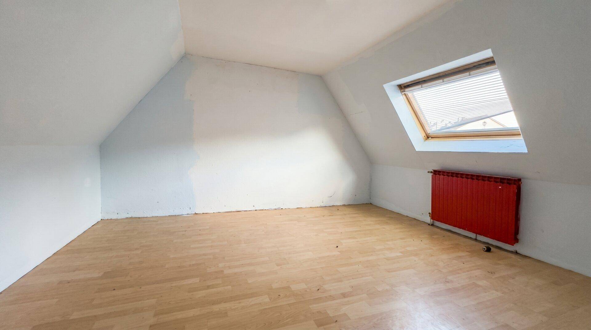 Dachgeschosszimmer mit schrägen Wänden, Laminatboden und Dachfenster, das renoviert werden muss.