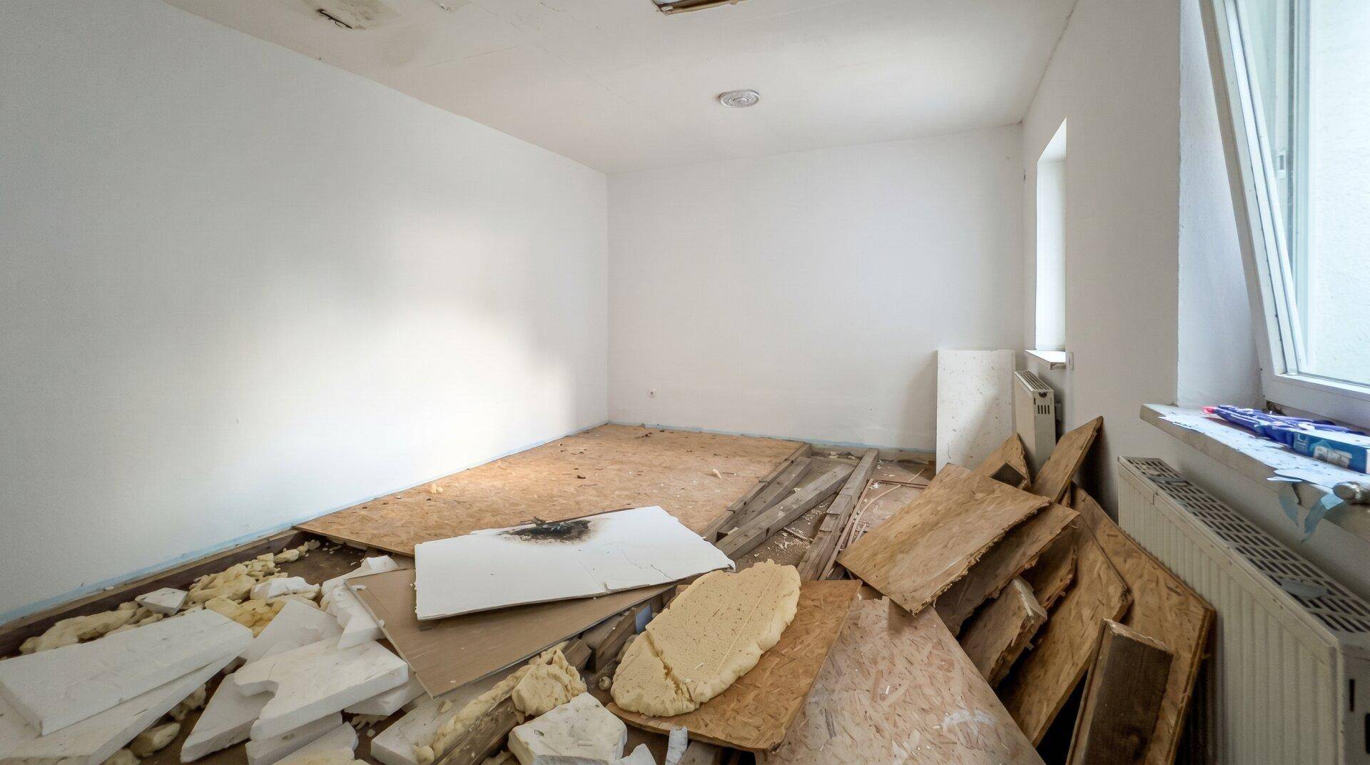 Renovierungsbedürftiges Schlafzimmer mit weißen Wänden und Fenster, bereit für die Neugestaltung.