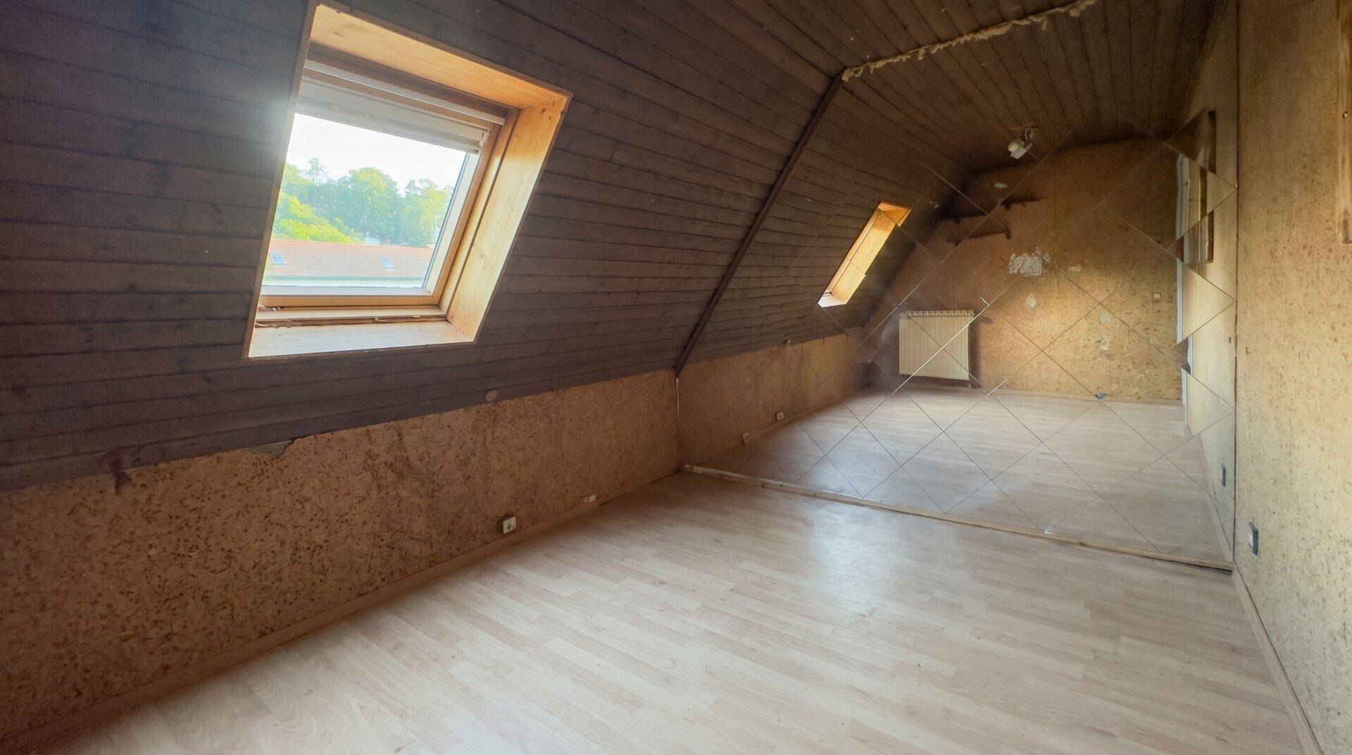 Dachgeschosszimmer mit Holzverkleidung, Laminatboden und Dachfenstern, das eine Renovierung benötigt.