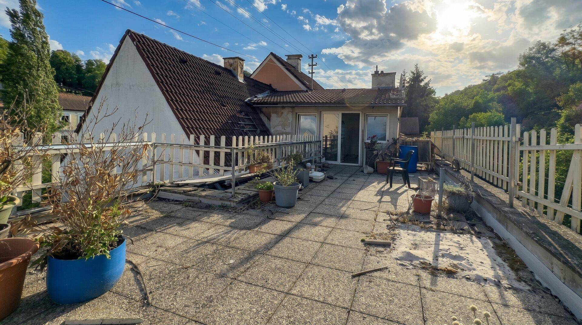 Große Außenterrasse mit Betonplatten und Zaun, die eine Renovierung und Gestaltung benötigt.