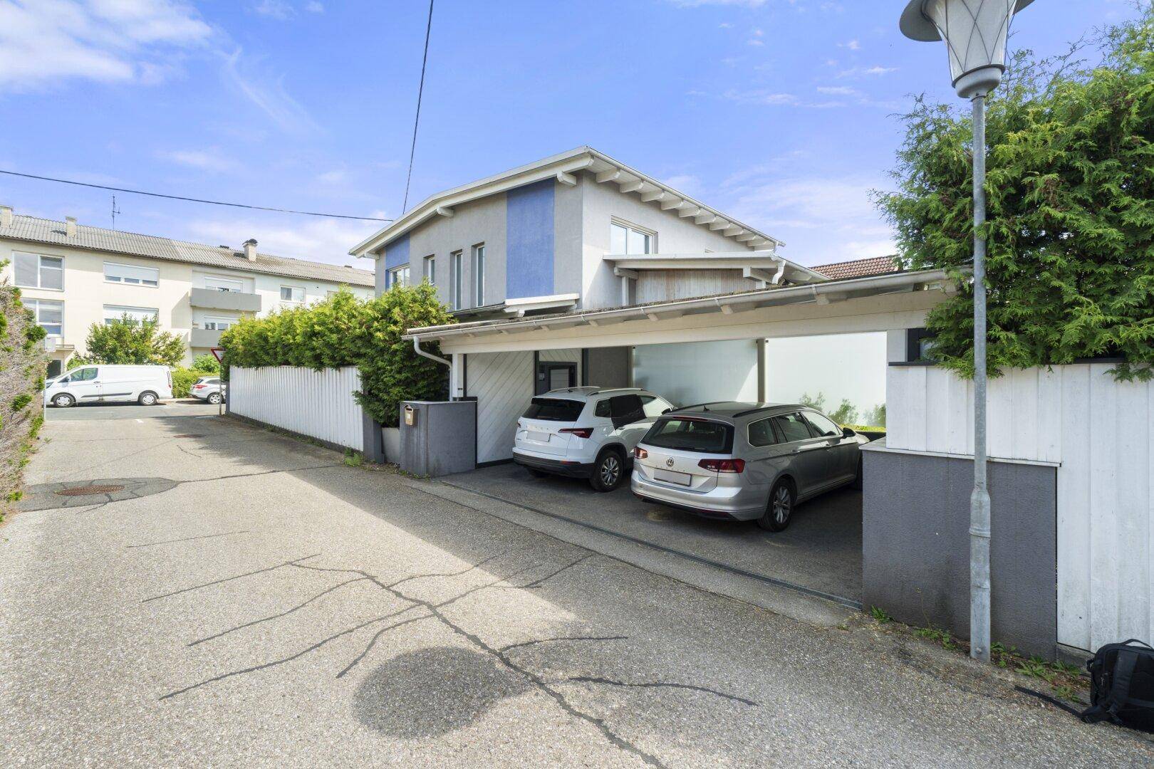 Ansicht des Hauses von der Straße mit überdachtem Carport und geparkten Fahrzeugen.
