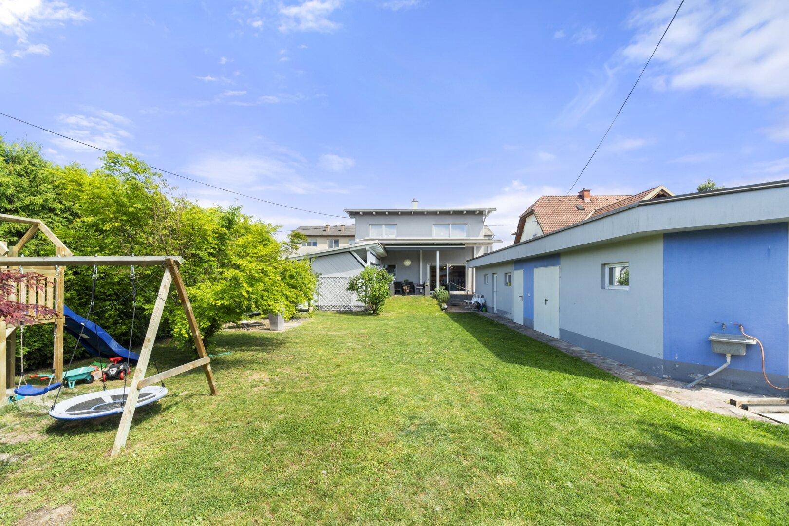 Großer, gepflegter Garten mit Rasenfläche, Spielgeräten und Blick auf die Rückseite des Hauses.