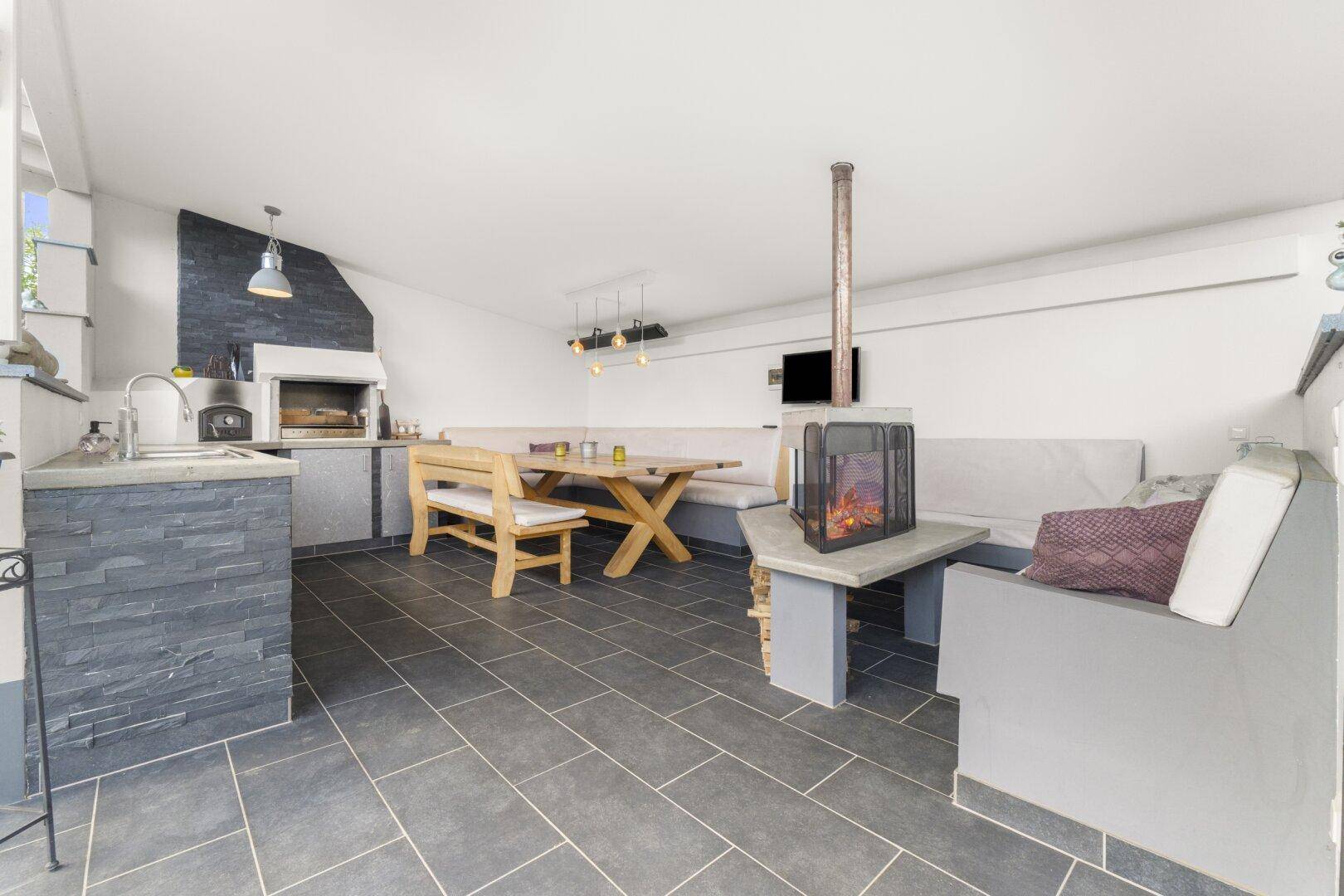 Geräumige überdachte Terrasse mit langer Sitzbank, Esstisch und dekorativem Kamin für entspannte Stunden.
