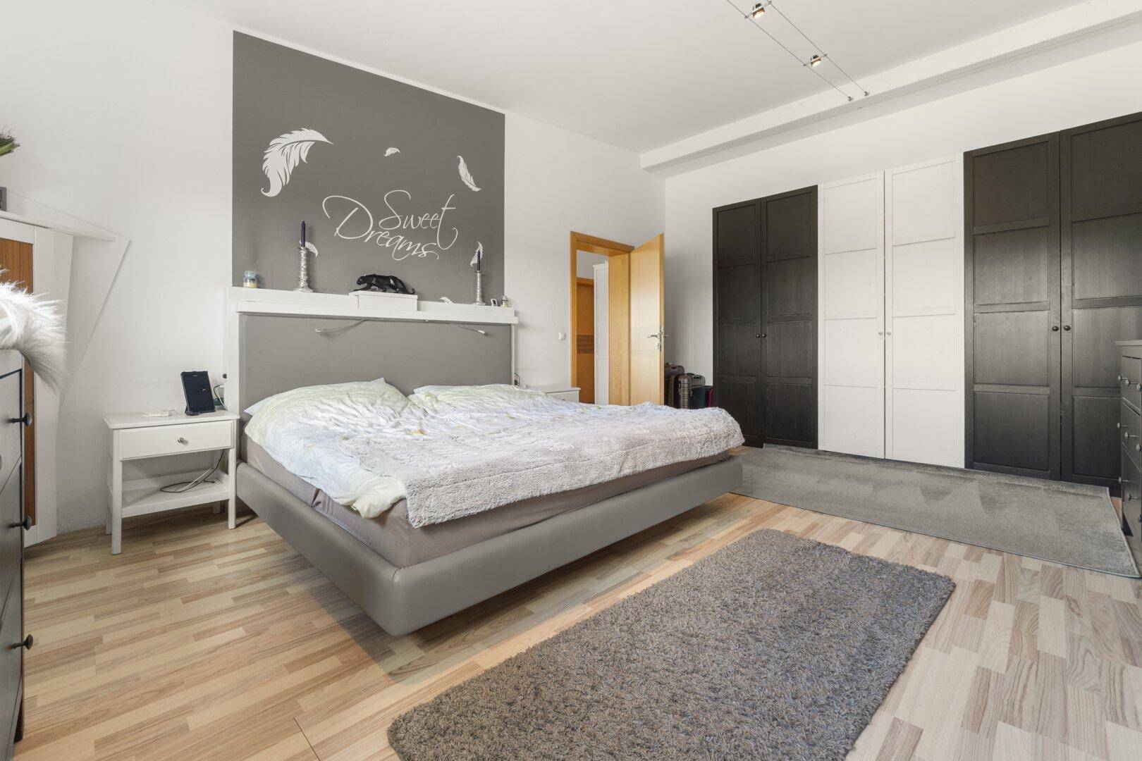 Geräumiges Schlafzimmer mit modernem Bett, integrierten Kleiderschränken und hellem Holzfußboden.
