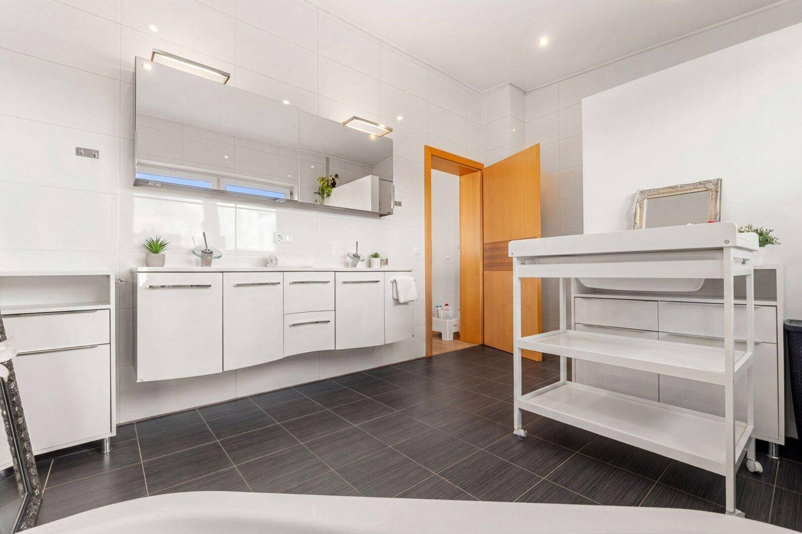 Modernes Badezimmer mit großem Doppelwaschtisch, Spiegelschrank und dunklen Bodenfliesen.