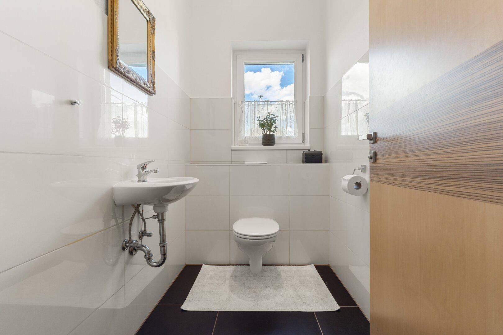 Helles Gäste-WC mit kleinem Waschbecken, Toilette und Fenster für natürliche Belüftung.