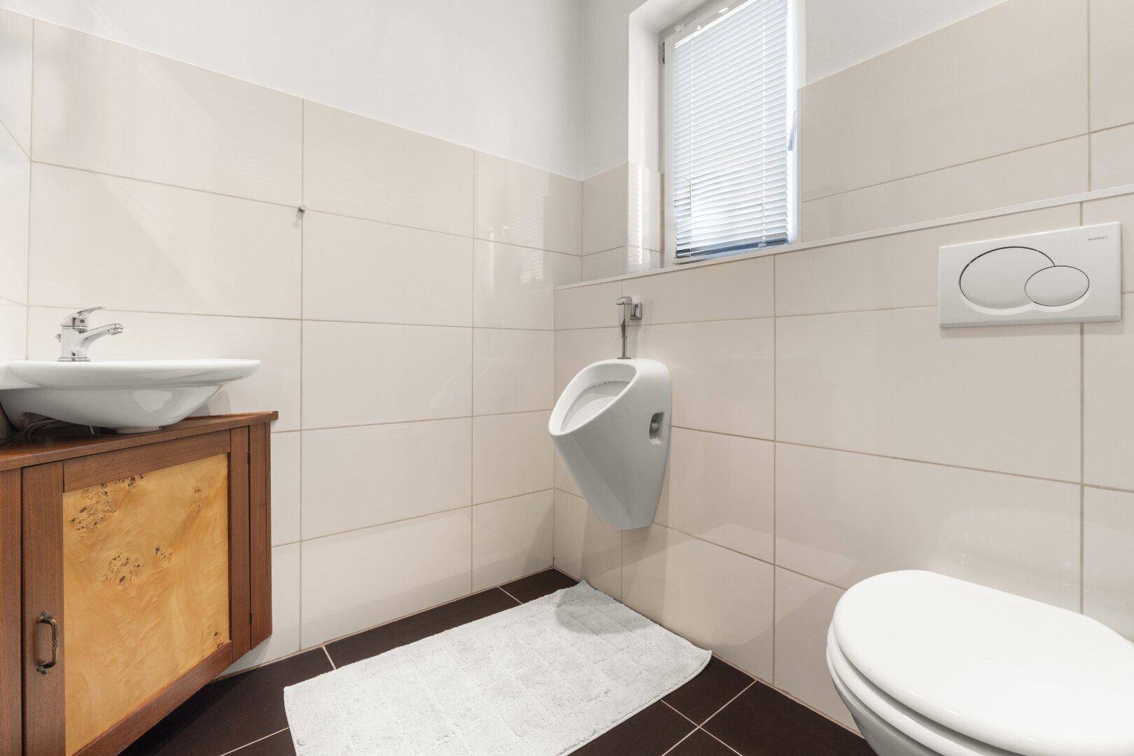 Modernes Gäste-WC mit Urinal, Waschbecken und Fenster für optimale Belüftung.