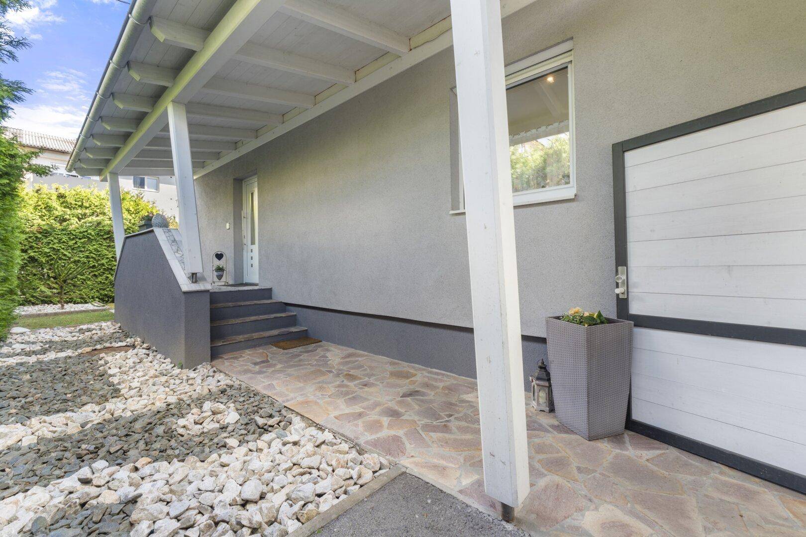 Überdachter Eingangsbereich eines Hauses mit Steintreppe, Natursteinplatten und einem gepflegten Vorgarten.