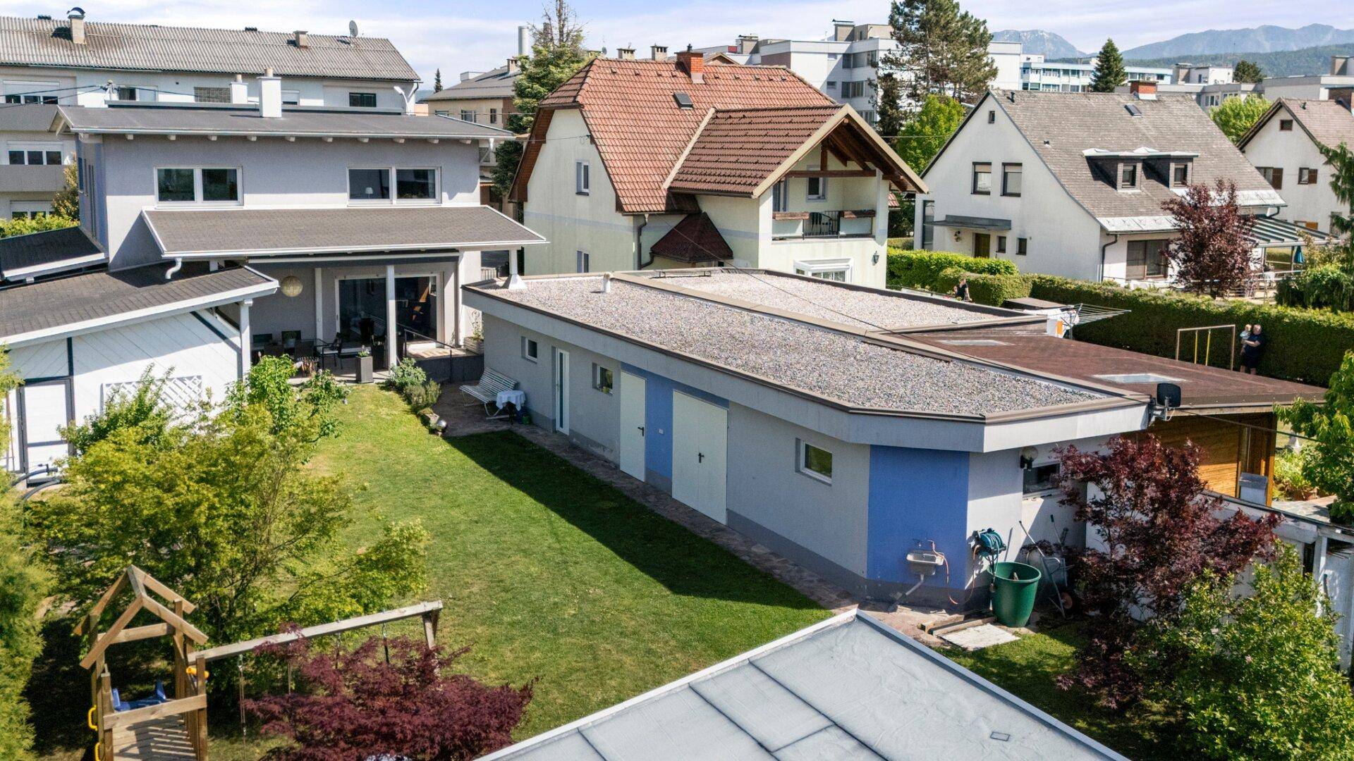 Luftaufnahme des Hauses mit großem Garten, Spielplatz und angrenzendem Nebengebäude in einer Wohnsiedlung.