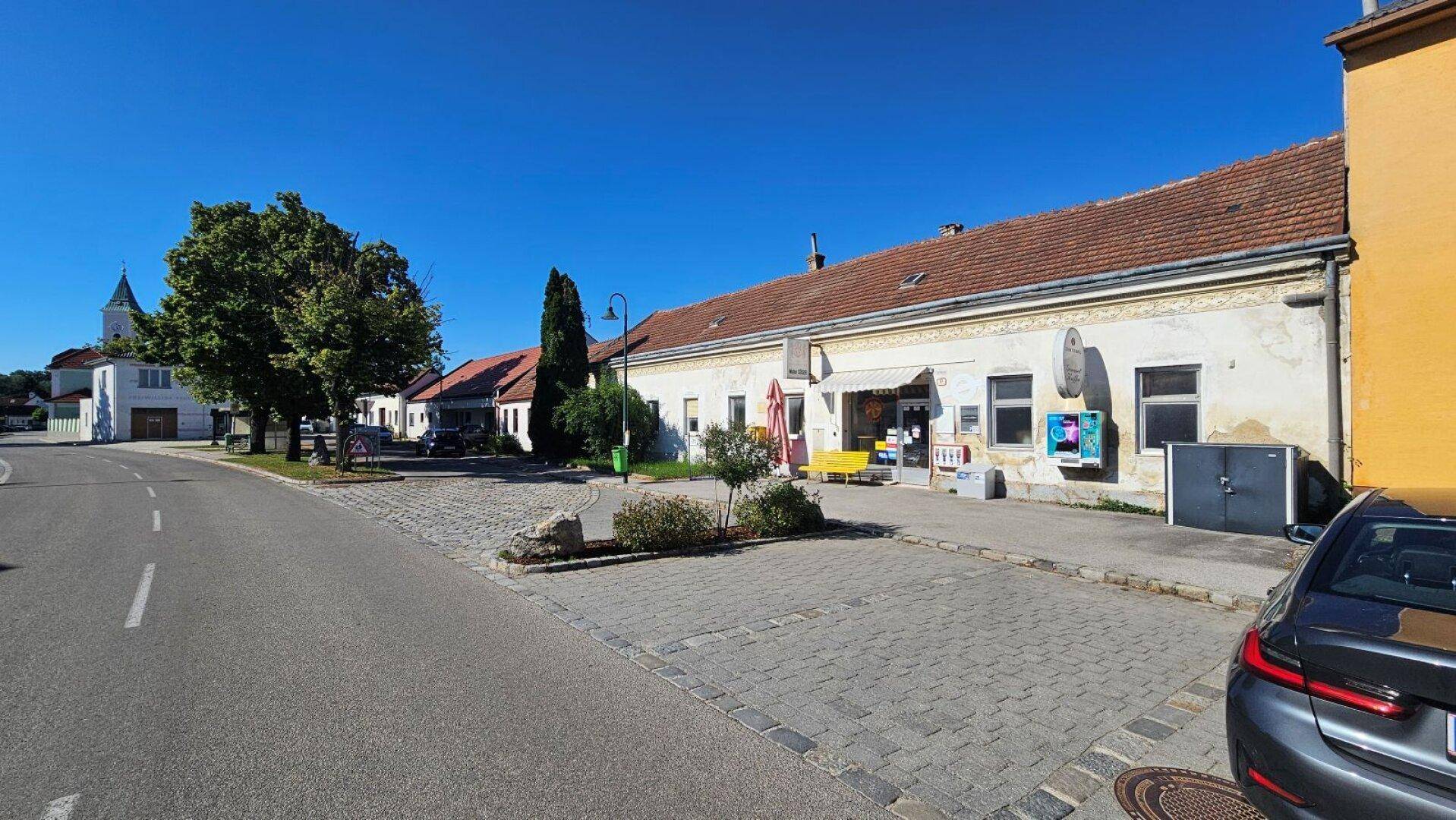 Weitläufige Ansicht des Gebäudes mit Straße, Parkplatz und Kirchturm im Hintergrund.
